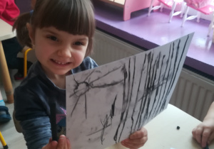 Dziewczynka pokazuje rysunek namalowany węglem